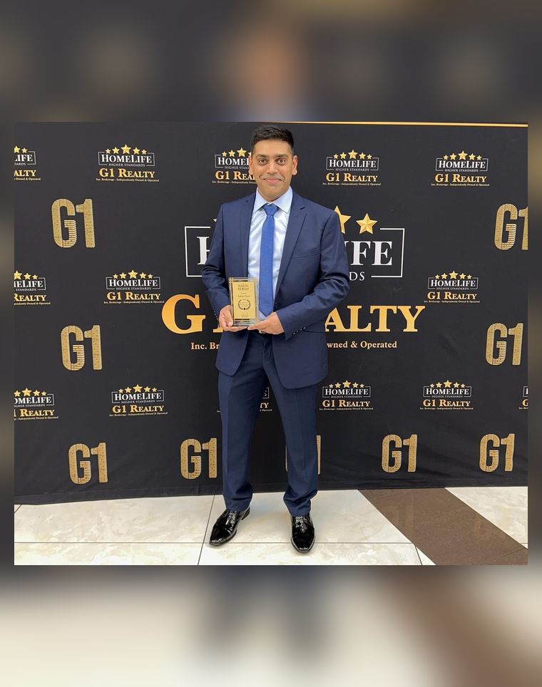 Robin Patel holding a plaque in front of a gold and black HomeLife G1 Realty step-and-repeat backdrop.