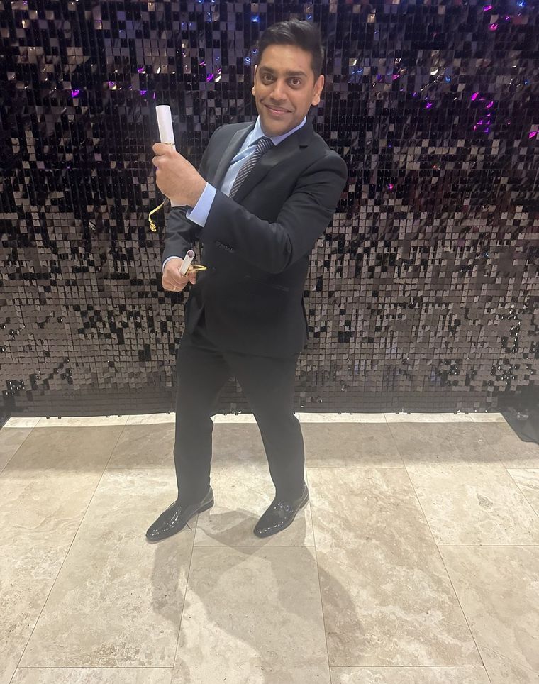 Robin Patel holding an award in front of a lit backdrop at an awards evening.