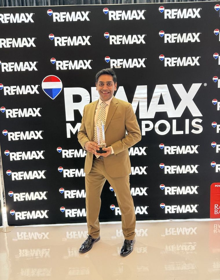 Robin Patel holding an award in front of a RE/MAX Metropolis Realty backdrop.